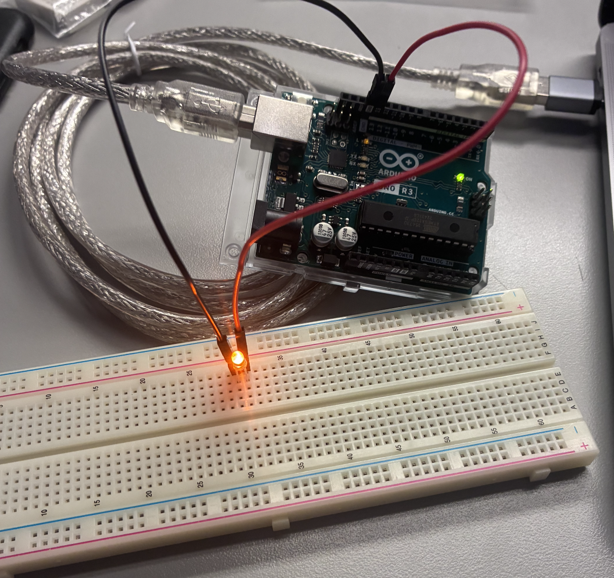 A single LED glows on a breadboard as a m-m jumper connects it to the Arduino.